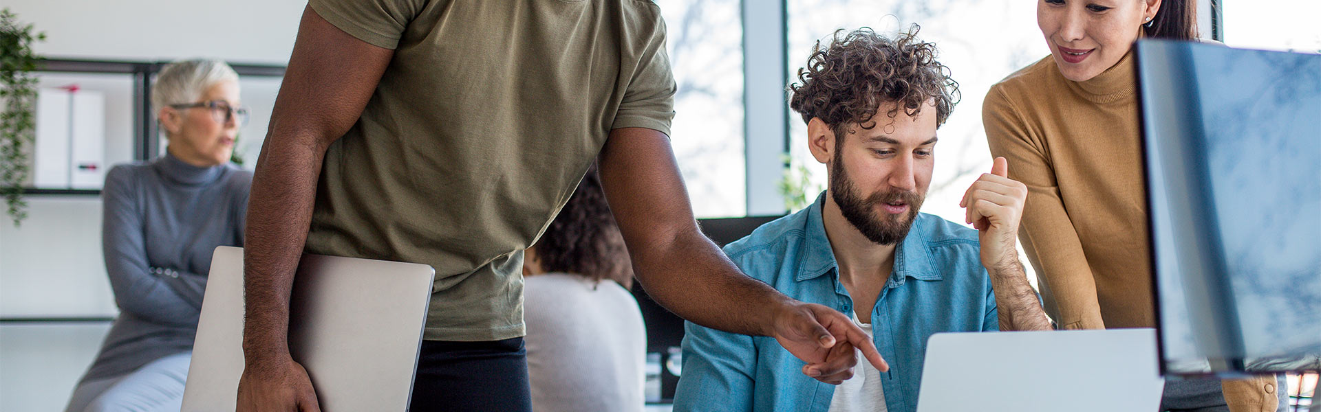 Man helping fellow colleagues by pointing at laptop screen